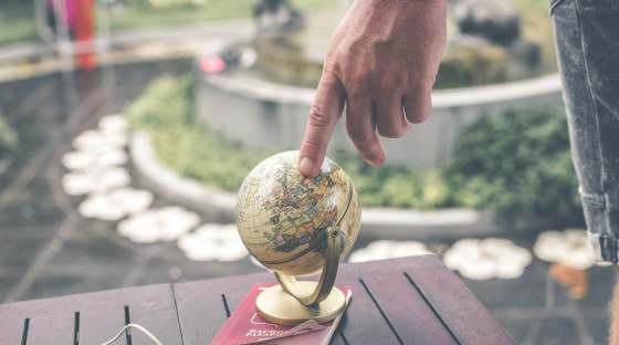 Person with finger on a small globe which is on a passport