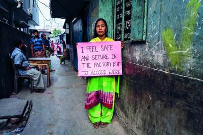 Image: bangladeshi garment worker holding sign that reads i feel safe and secure in the factory due to accord work