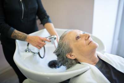 Person with grey hair having hair washed over sink by someone else