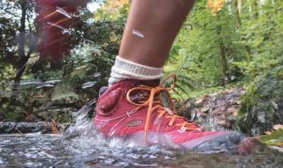 Person wearing red trainer outdoor shoe stepping into puddle