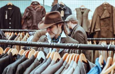 Man wearing hat browsing jackets with other clothes hanging up behind