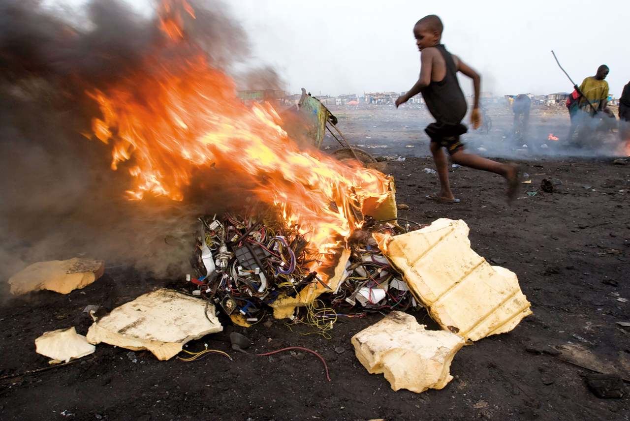 child in Accra, Ghana, runs next to a fire where electronic cables and other electrical components are being burned in order to melt off the plastic and reclaim the copper wiring