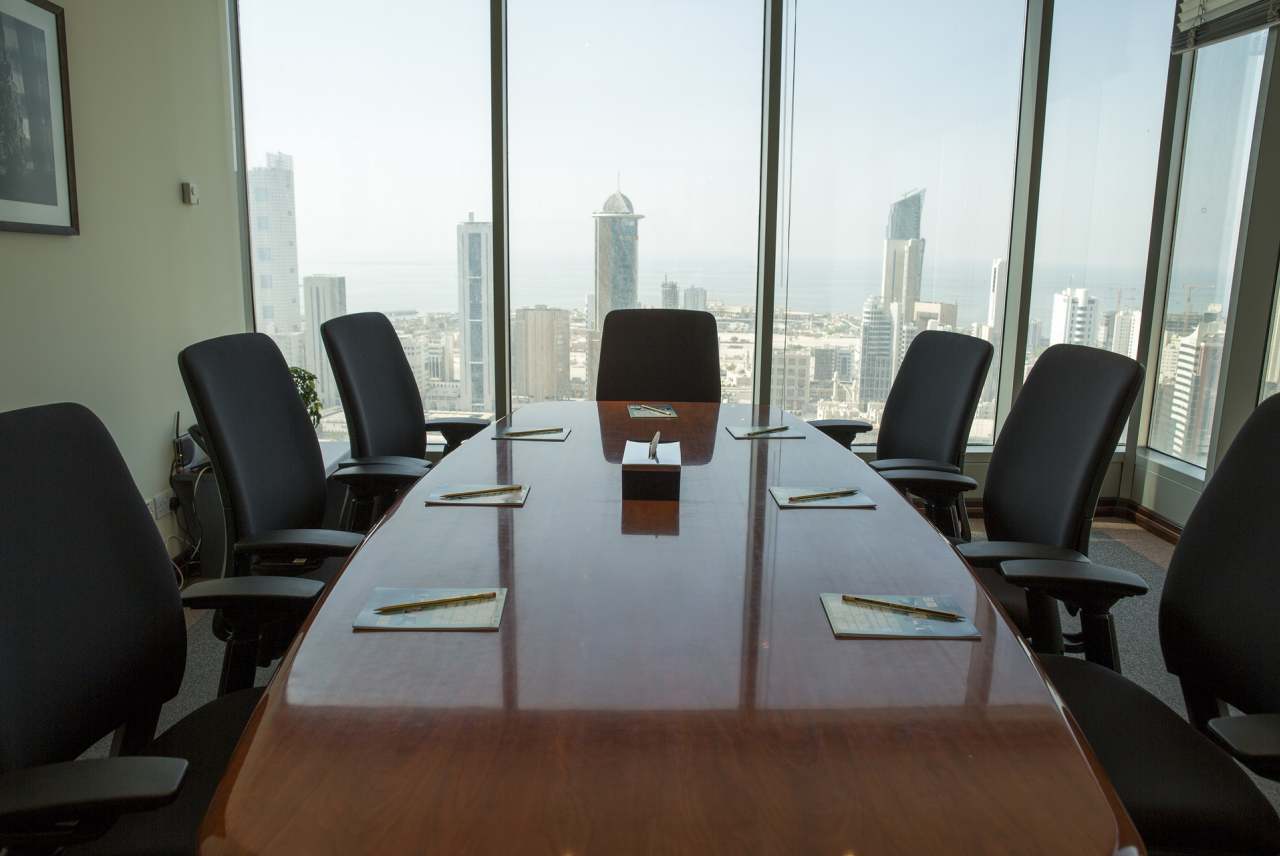 View down a table with chairs either side and window looking out to city skyscraper towers