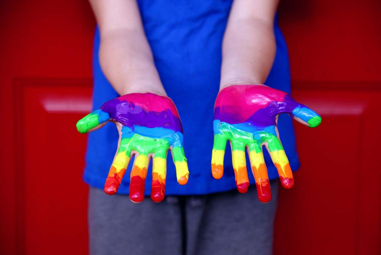 Person showing palms of hands painted with rainbow colours of paint
