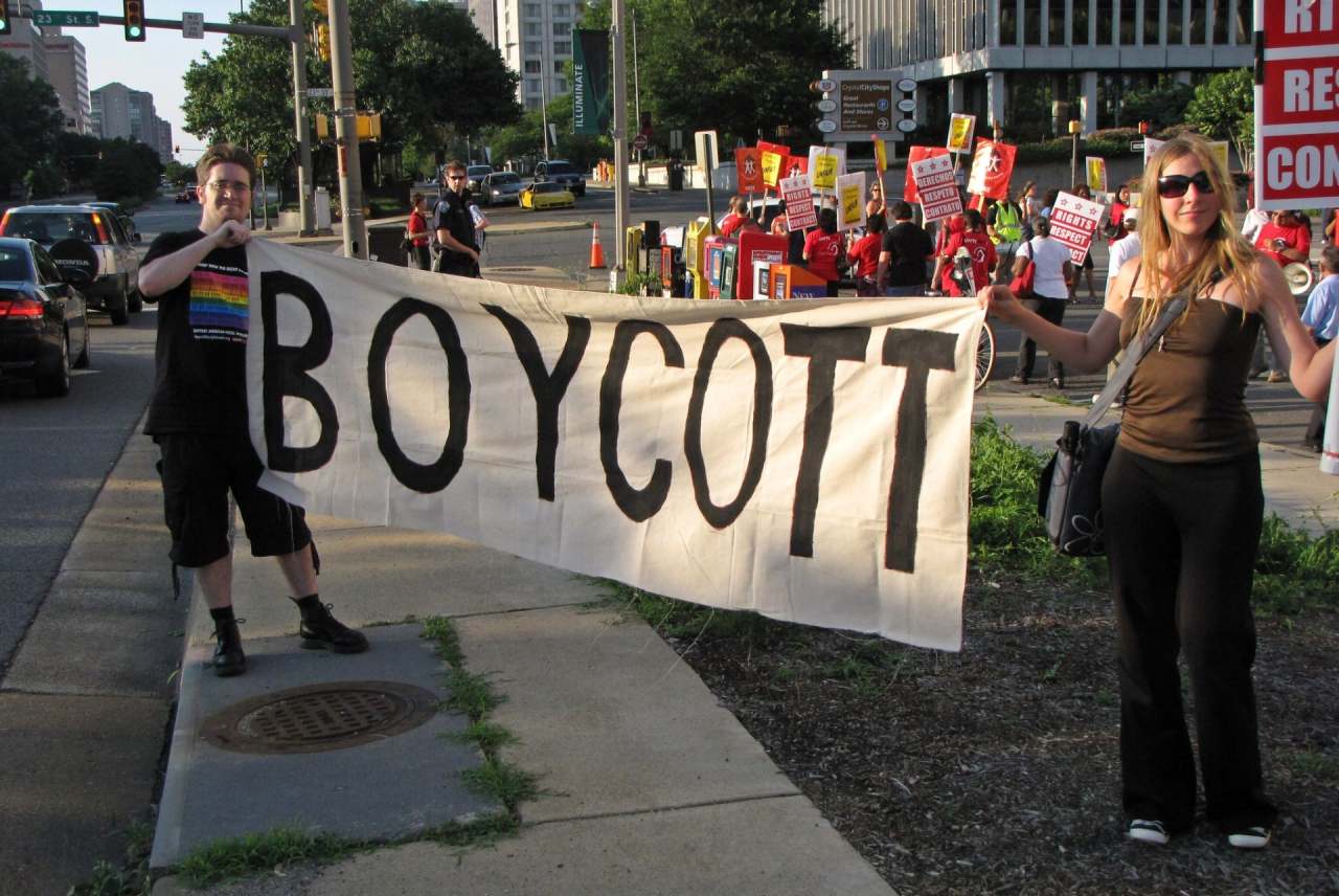 Two people holding banner which reads 'Boycott' with crowd behind