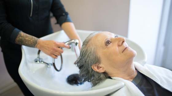 Person with grey hair having hair washed over sink by someone else