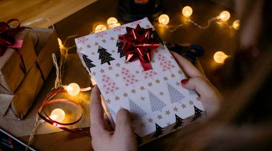 Person holding wrapped Christmas gift, with sparkly lights in background