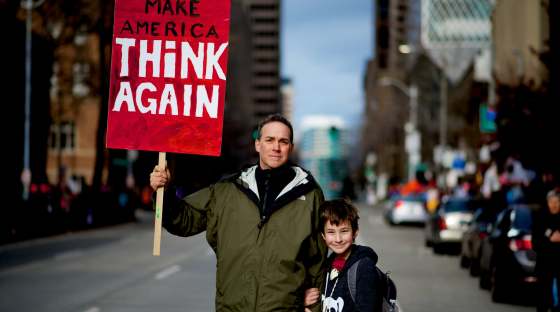 Man and boy on street holding sign which reads 'Make America Think Again'