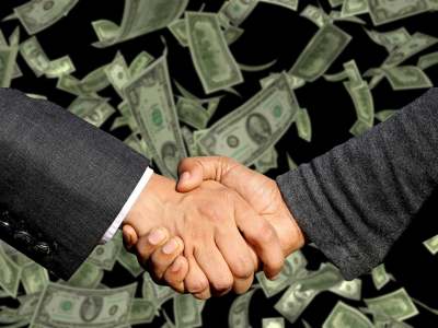 Handshake between two male hands with paper cash money in background
