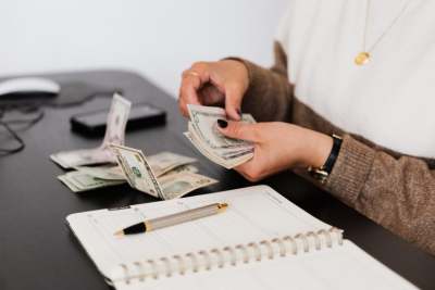Person counting money on desk with notepad