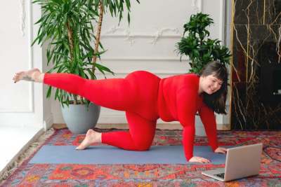 Large woman in sportswear doing yoga at home with laptop