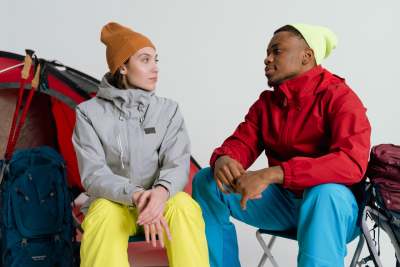 Woman and man sitting in a studio in outdoor clothing with tent behind