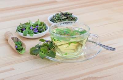 Clear glass cup with fresh herbs in it and saucers of fresh herbs on table