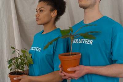 Woman and man wearing blue t-shirts with the word 'volunteer' on them, each holding a plant in front of them