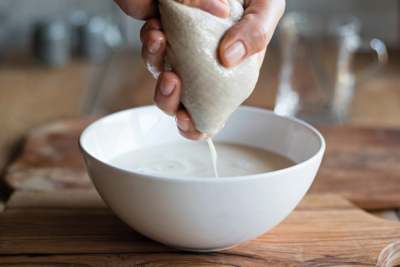 Hand squeezing bag of oat pulp above bowl of liquid