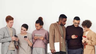 Six people standing in a line all looking at mobile phones or tablet devices