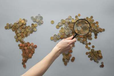 Map of world made out of coins, with person holding magnifying glass over part of the worldy