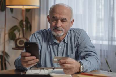 Older man looking at phone and credit card sat at table