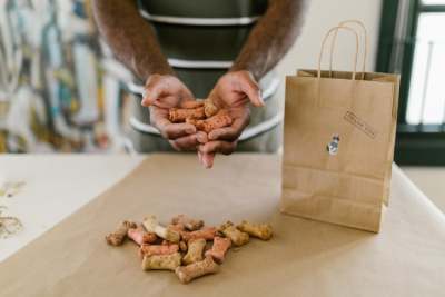 Person holding dried dog biscuits in hand with brown paper bag on table