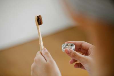 Person holding wooden toothbrush and small tin of tooth tablets