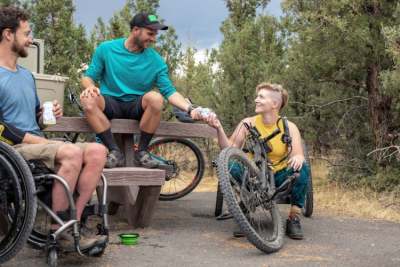 Three cyclists sitting together, two in adapted wheelchair bikes