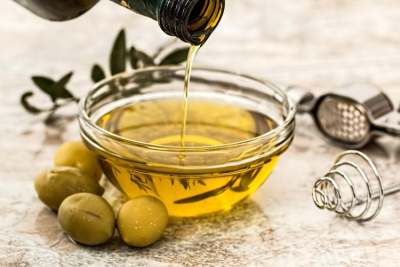 Olive oil being poured into a clear bowl, with olives on the table