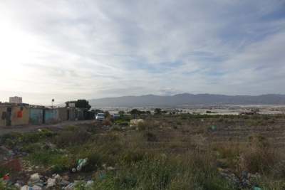 Landscape of wasteland with row of shacks alongside dirt track