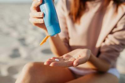 Woman sitting on beach putting suncream on from blue plastic bottle