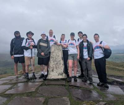 Group of people at trig point on top of a hill in wet weather