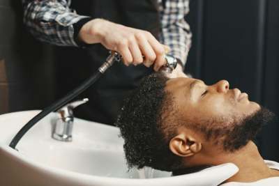 Person washing Black man's hair over sink
