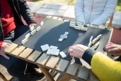 Three people playing dominoes on table outside in sunshine