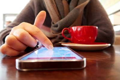 Person sitting in cafe scrolling on phone with cup of hot drink on table