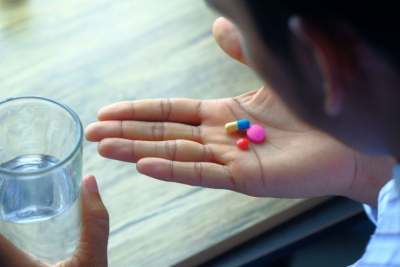 Three coloured pills on person's palm, with other hand holding glass of water