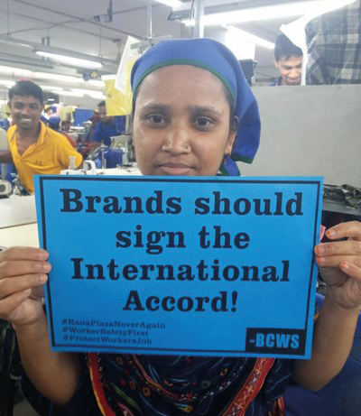 Person in clothing factory holding sign which reads 'Brands should sign the International Accord!'