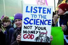 image: woman holding sign that reads listen to the science not your money god