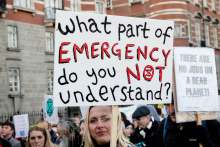 image: woman holding sign that reads what part of emergency do you not understand XR