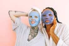 Two women with cosmetic skincare facemasks, wearing dressing gowns