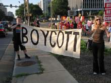 Two people holding banner which reads 'Boycott' with crowd behind