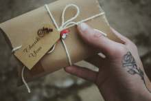 Hand holding a small brown packet with a 'thank you' label