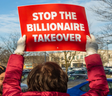 Back of person holding up placard: Stop the billionaire takeover