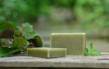 Two bars of green soap with nettle leaves and mint leaves around them