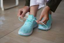 Person tying laces on pair of turquoise sneakers 