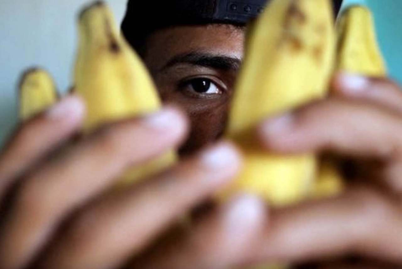 image: banana worker in focus with the bananas that he picks outstretched in front of him