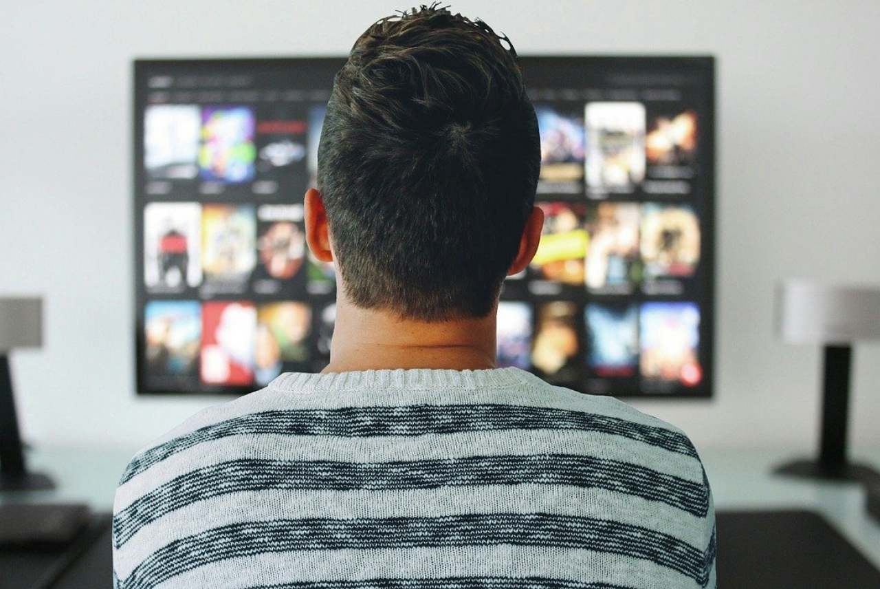Back of adult man watching tv screen