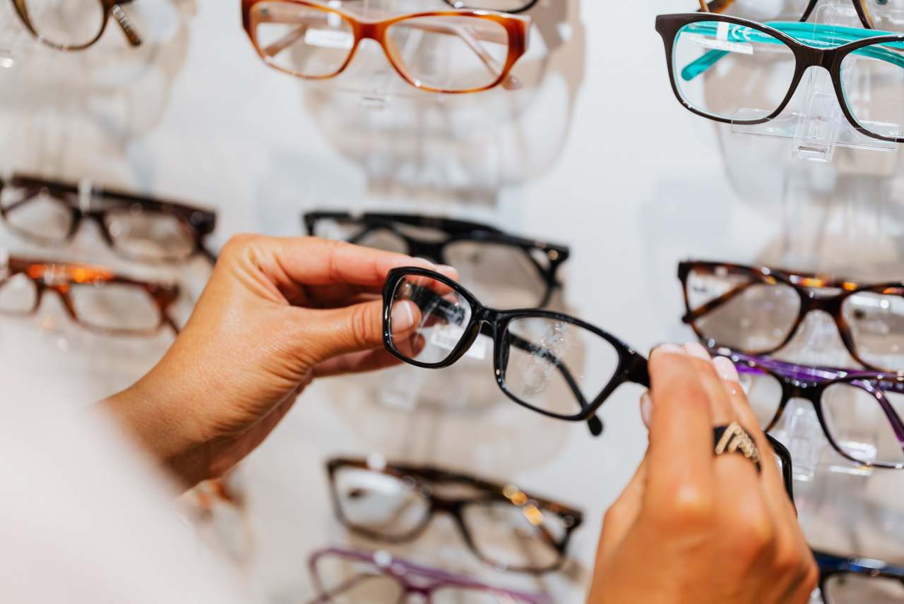 Person holding pair of glasses with shelf of glasses in background