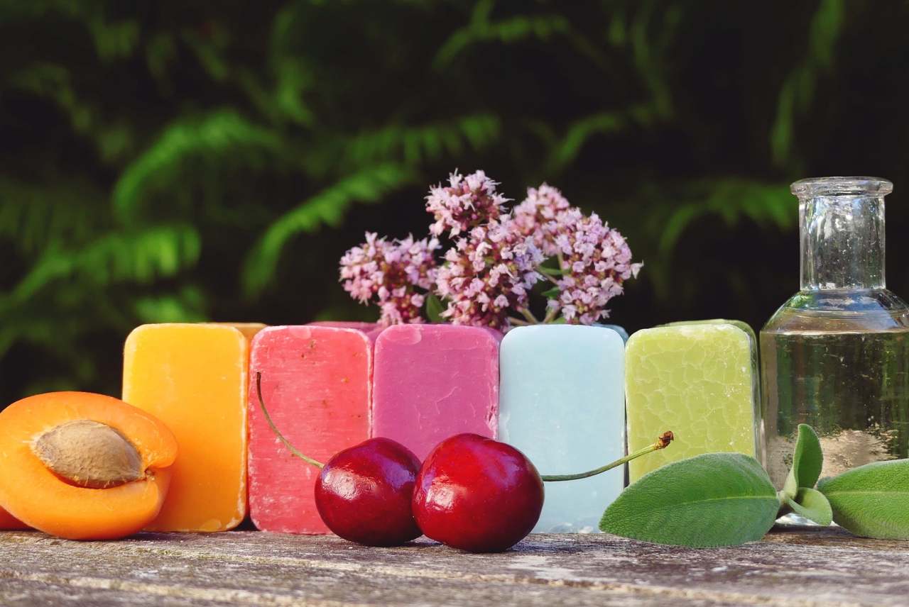 five bars of coloured soap with fruit and herbs next to them