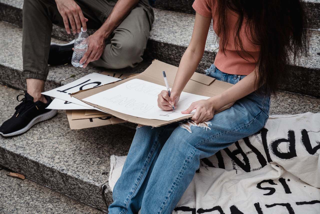 Two people sitting on steps making protest banner and placard