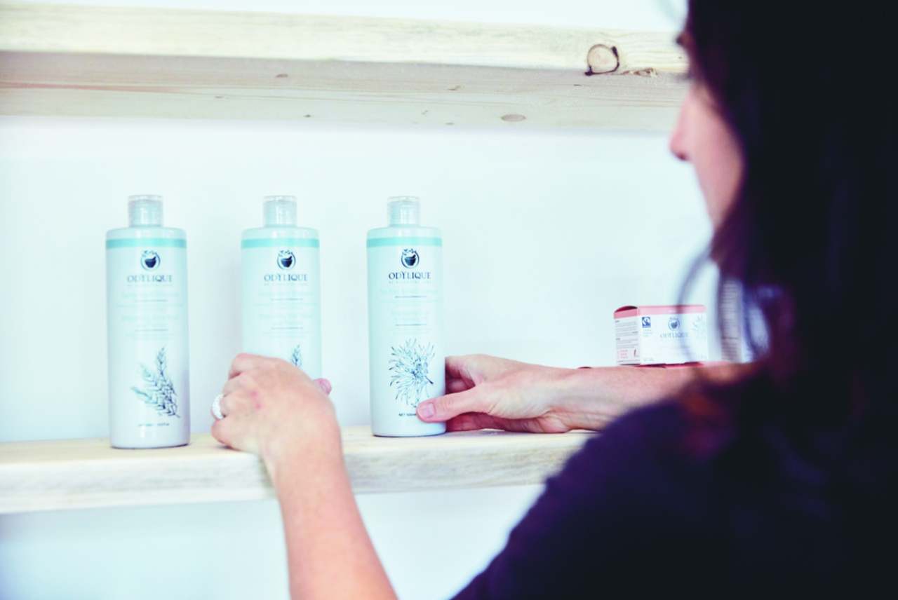 Odylique products on shelf with person holding the bottles