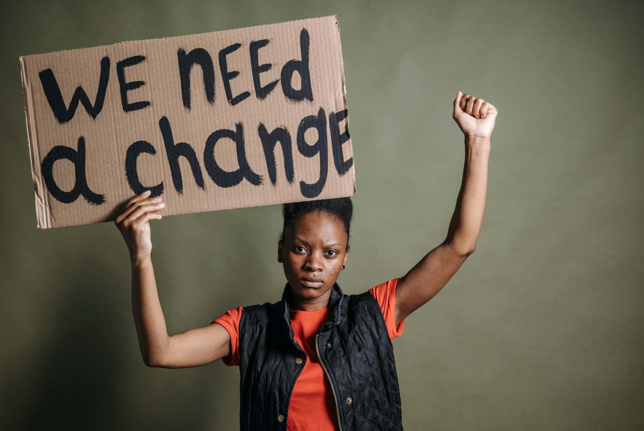 Woman holding banner which reads 'we need a change' with a raised clenched fist