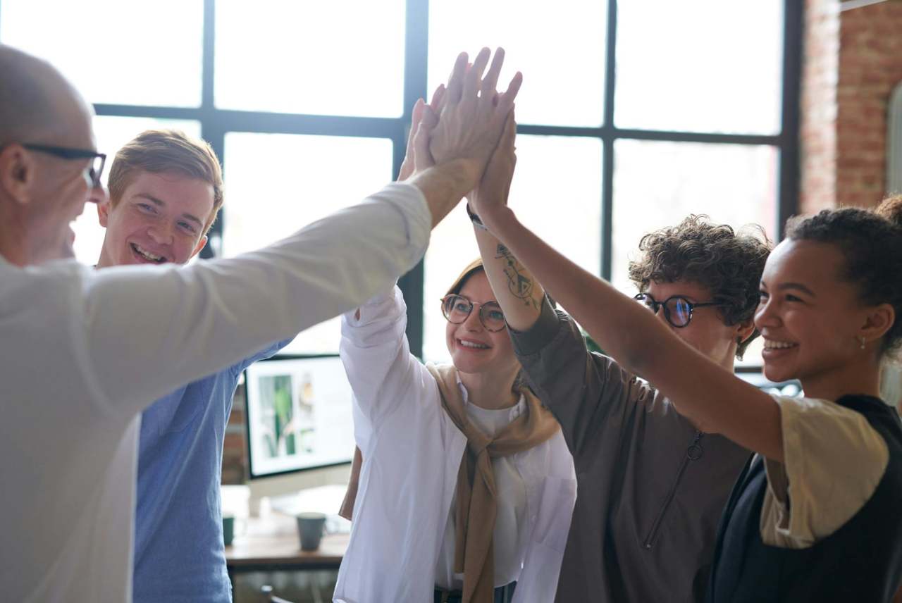 Group of five people with hands raised in high five position, together